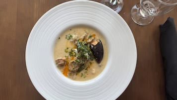 En hvid tallerken med cremet suppe, pyntet med krydderurter, på et træbord.