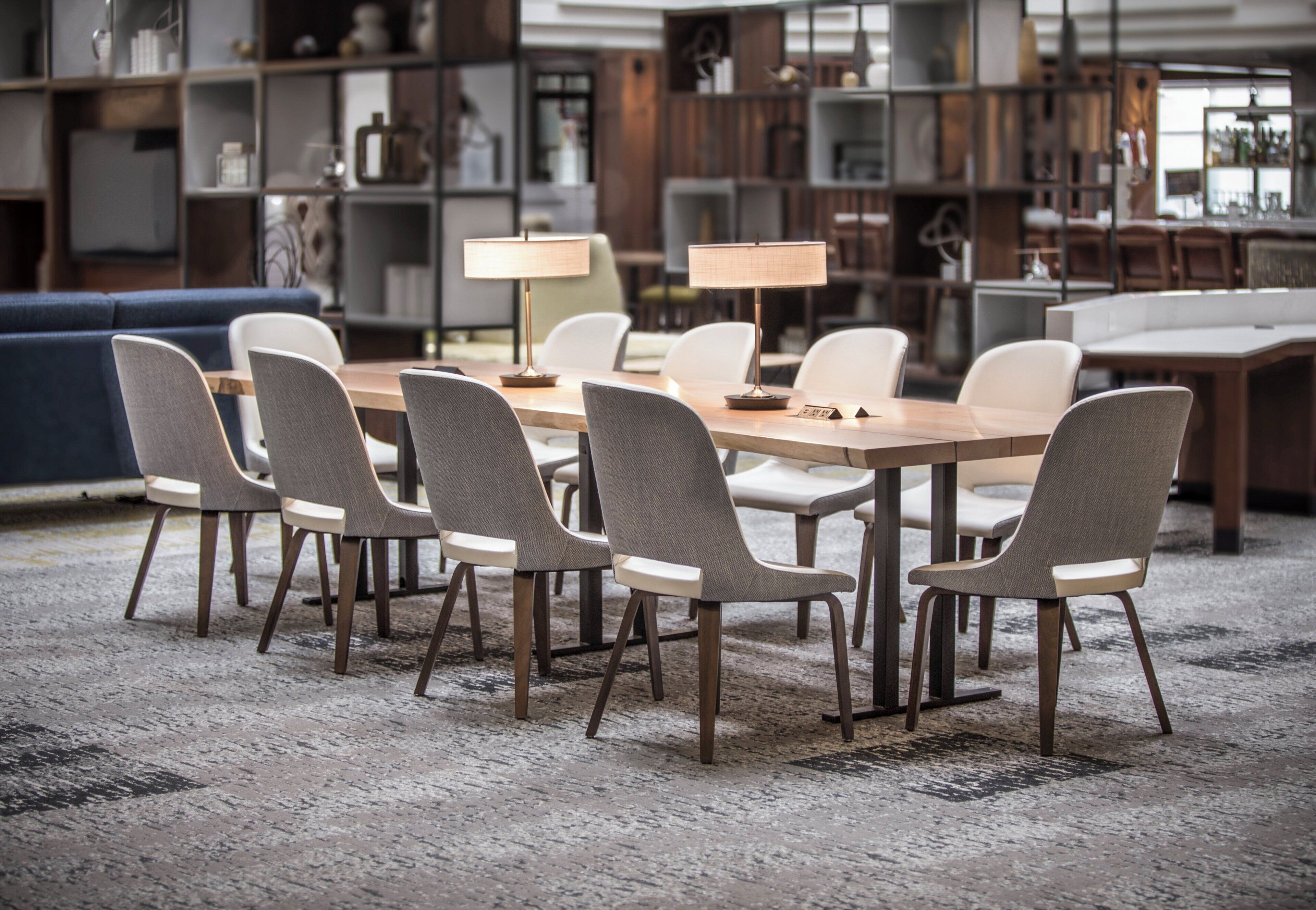 A modern dining area with a long table, six chairs, and two lamps.