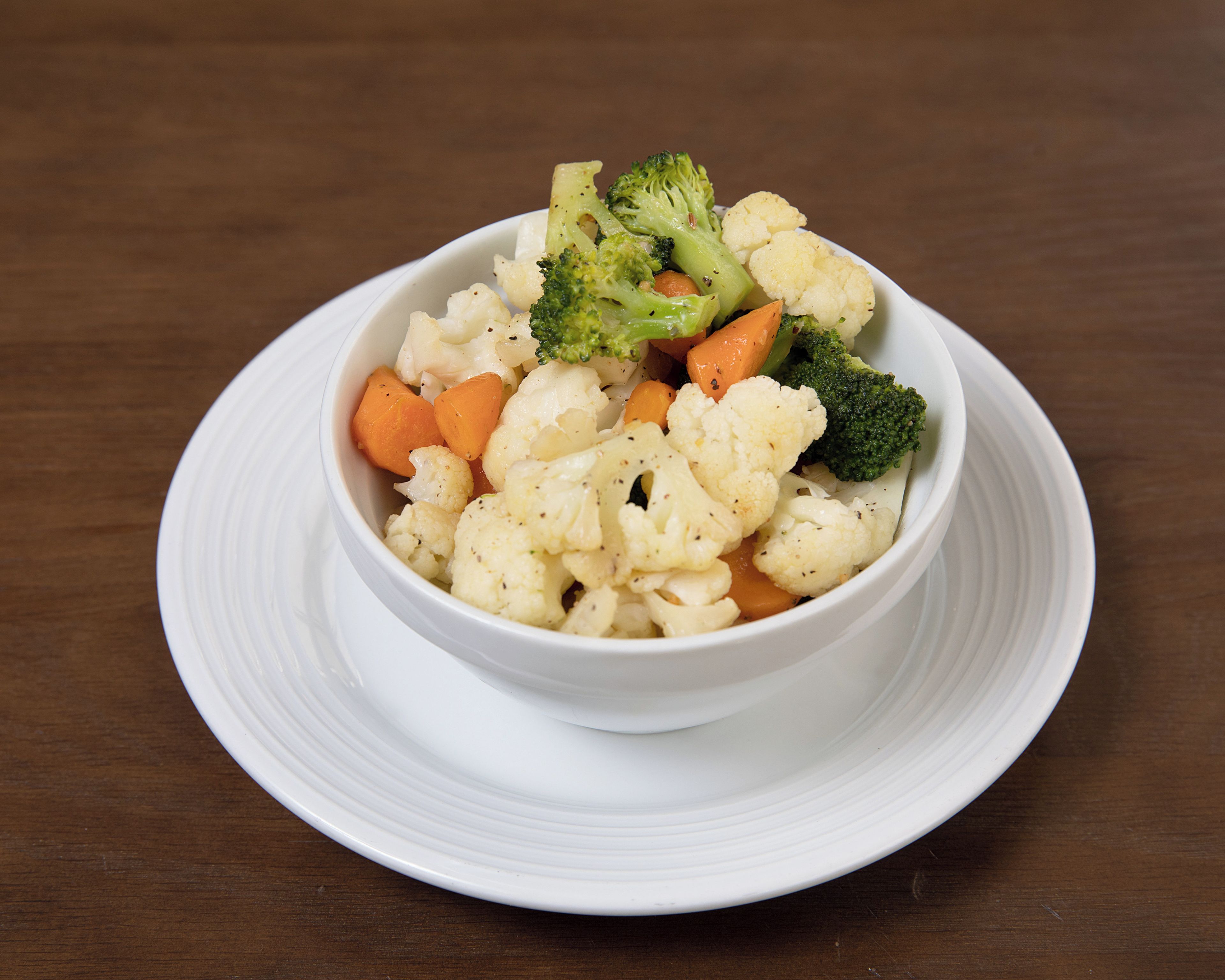 A white bowl of mixed vegetables on a white plate.