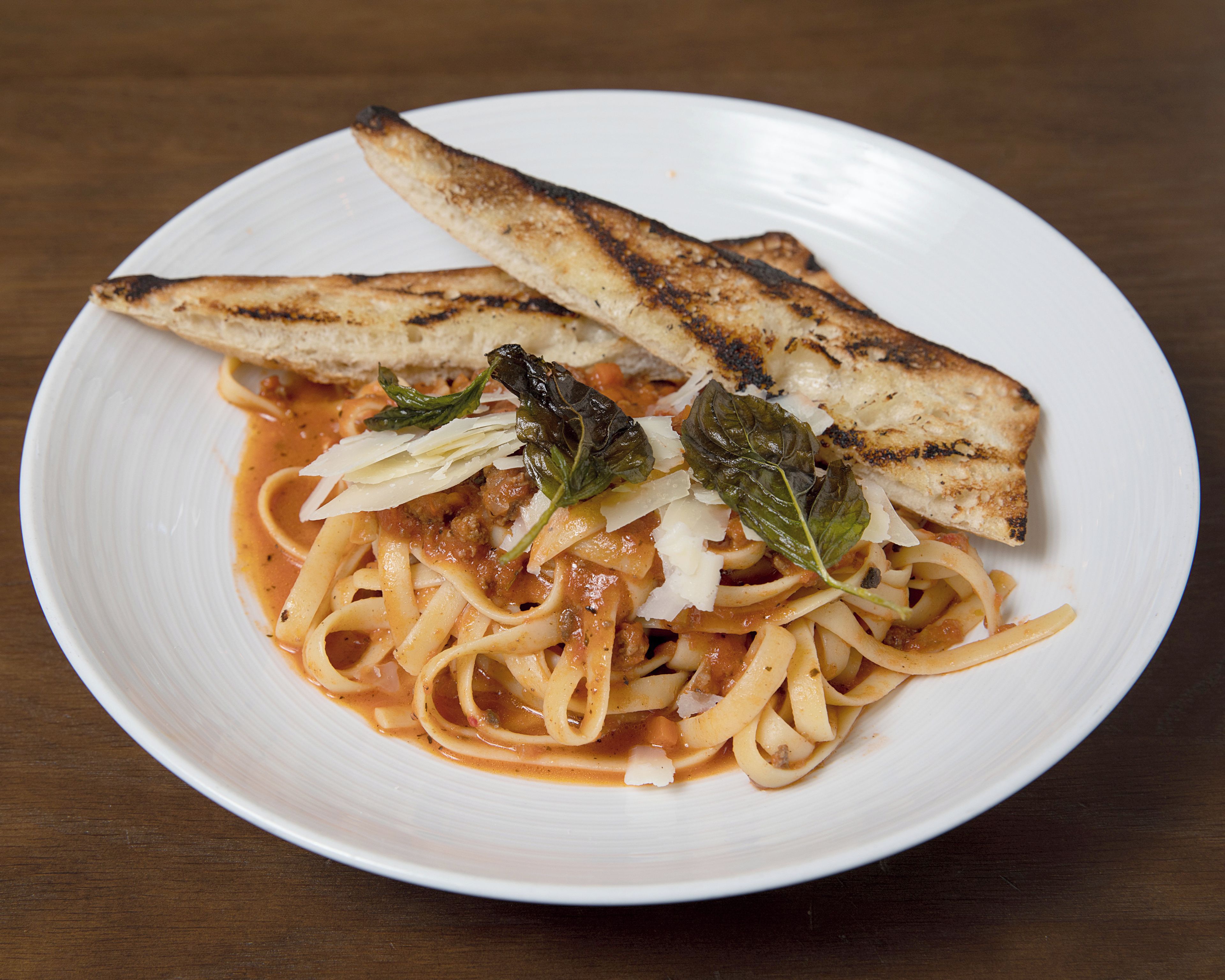 A plate of pasta with grilled bread and basil leaves.