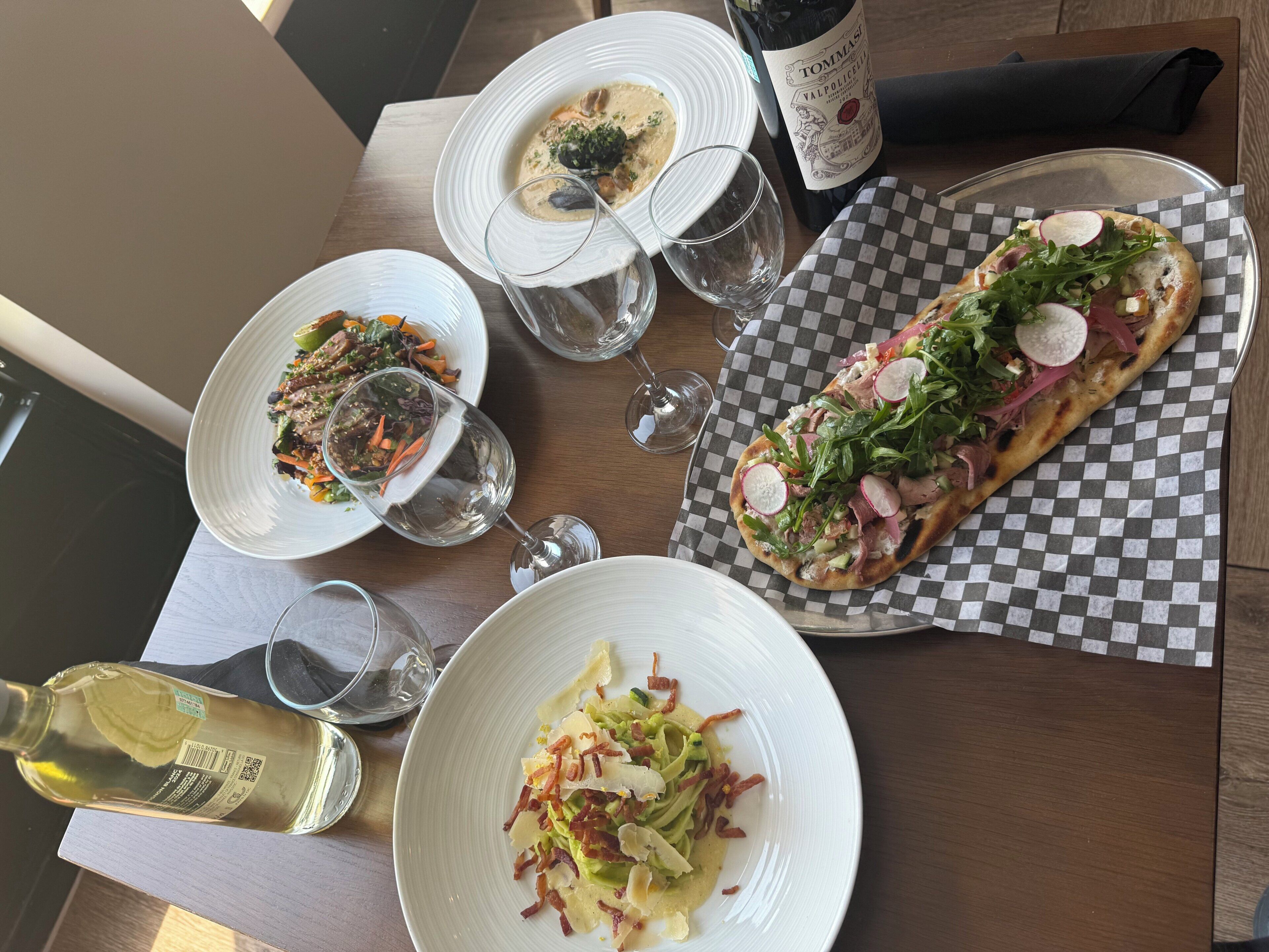 A dining table with plates of food, glasses, and a bottle of wine.