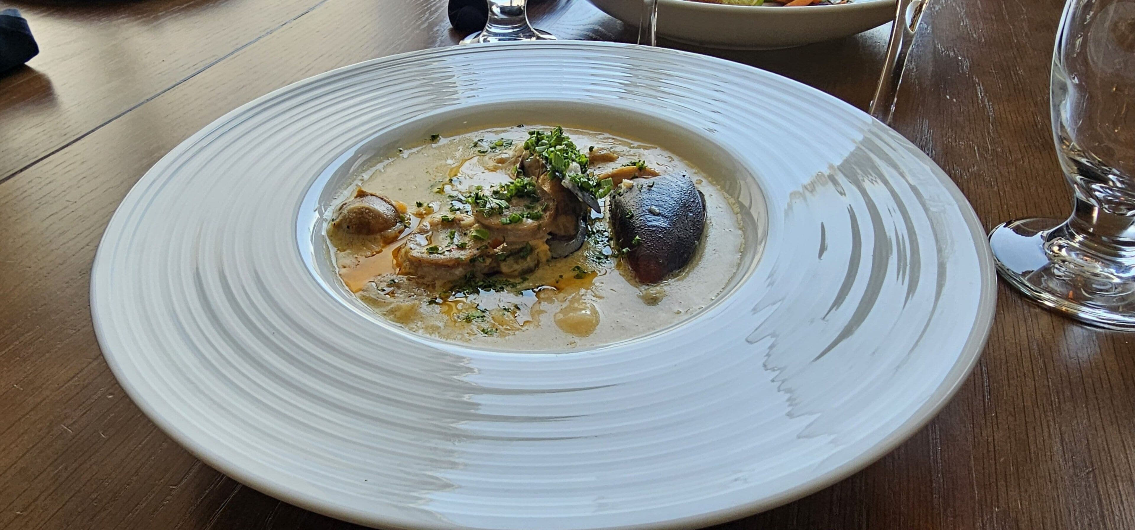 A white plate with a creamy dish, possibly fish, garnished with herbs, on a wooden table.