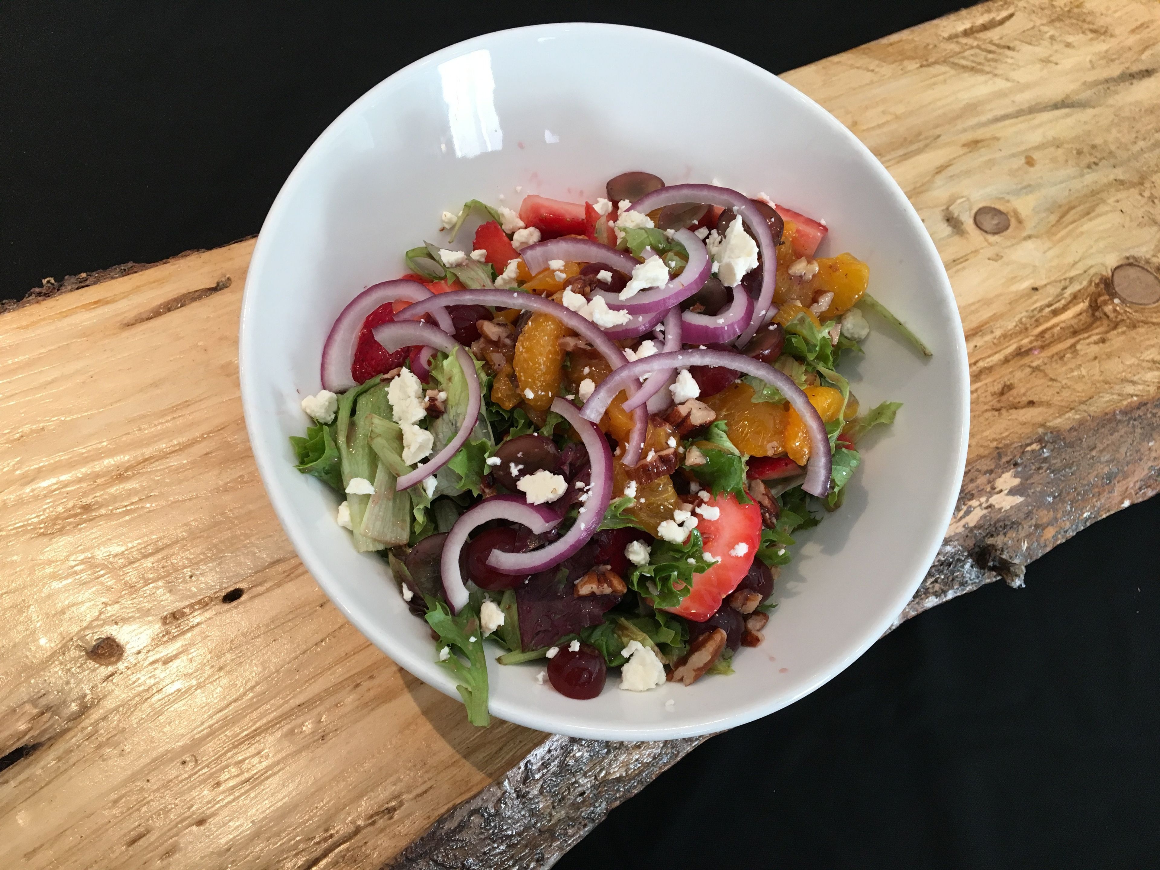 A white bowl of salad with various ingredients on a wooden surface.