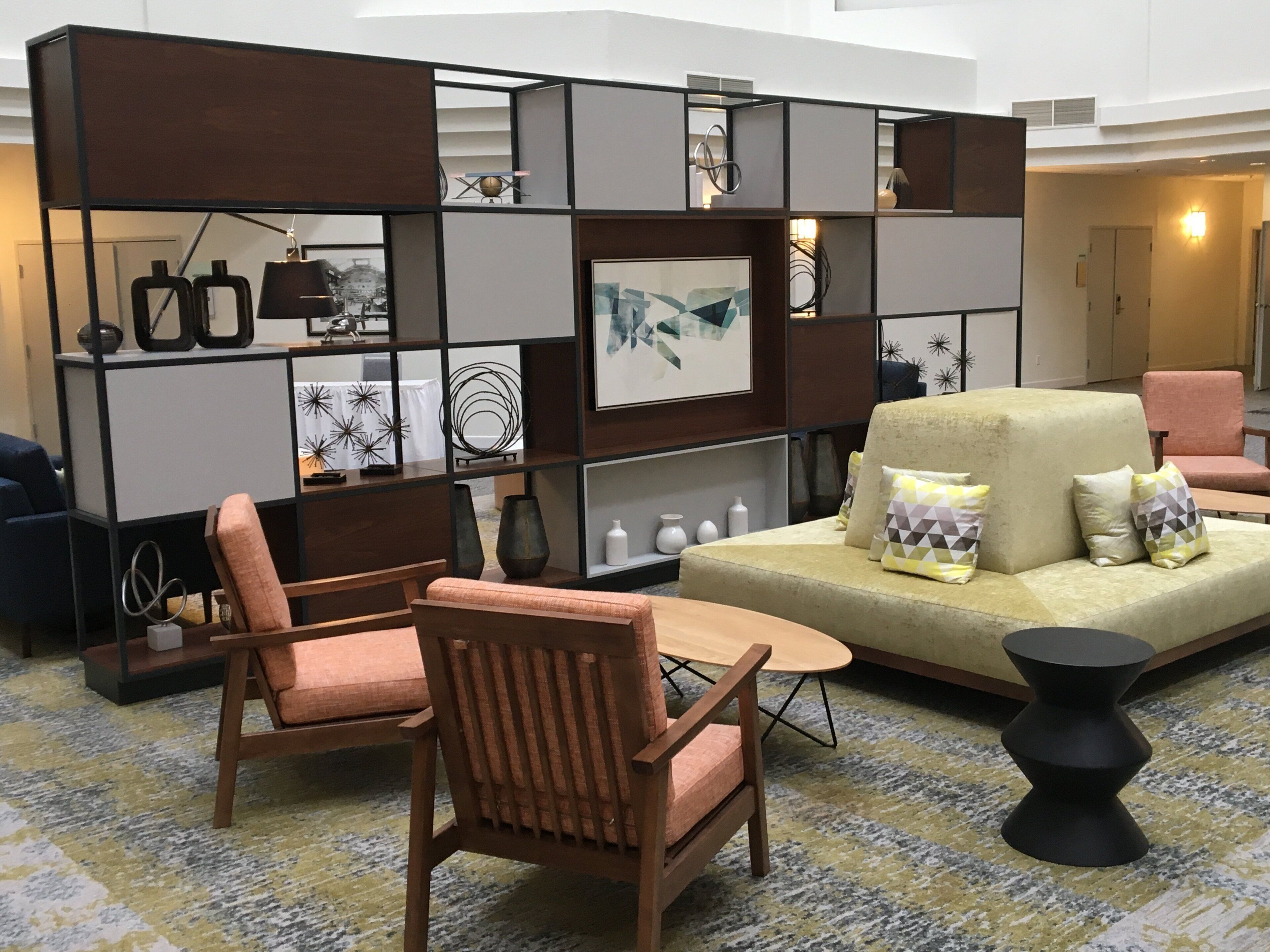 Een moderne woonkamer met een bank, stoelen, een salontafel en een decoratieve wandunit met planken en kunstwerken.