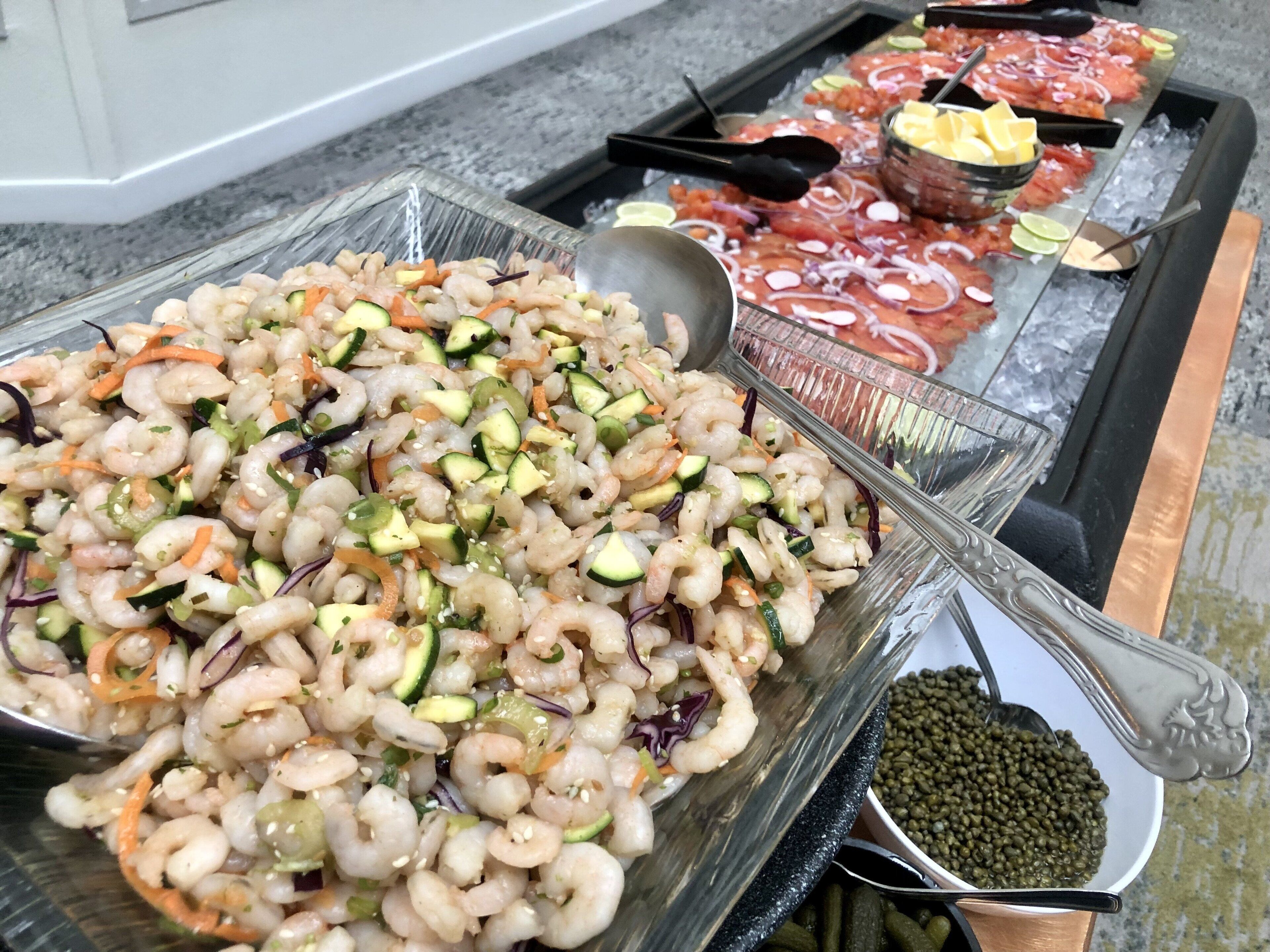 Un buffet proposant une salade de crevettes, du poisson cru et diverses sauces.