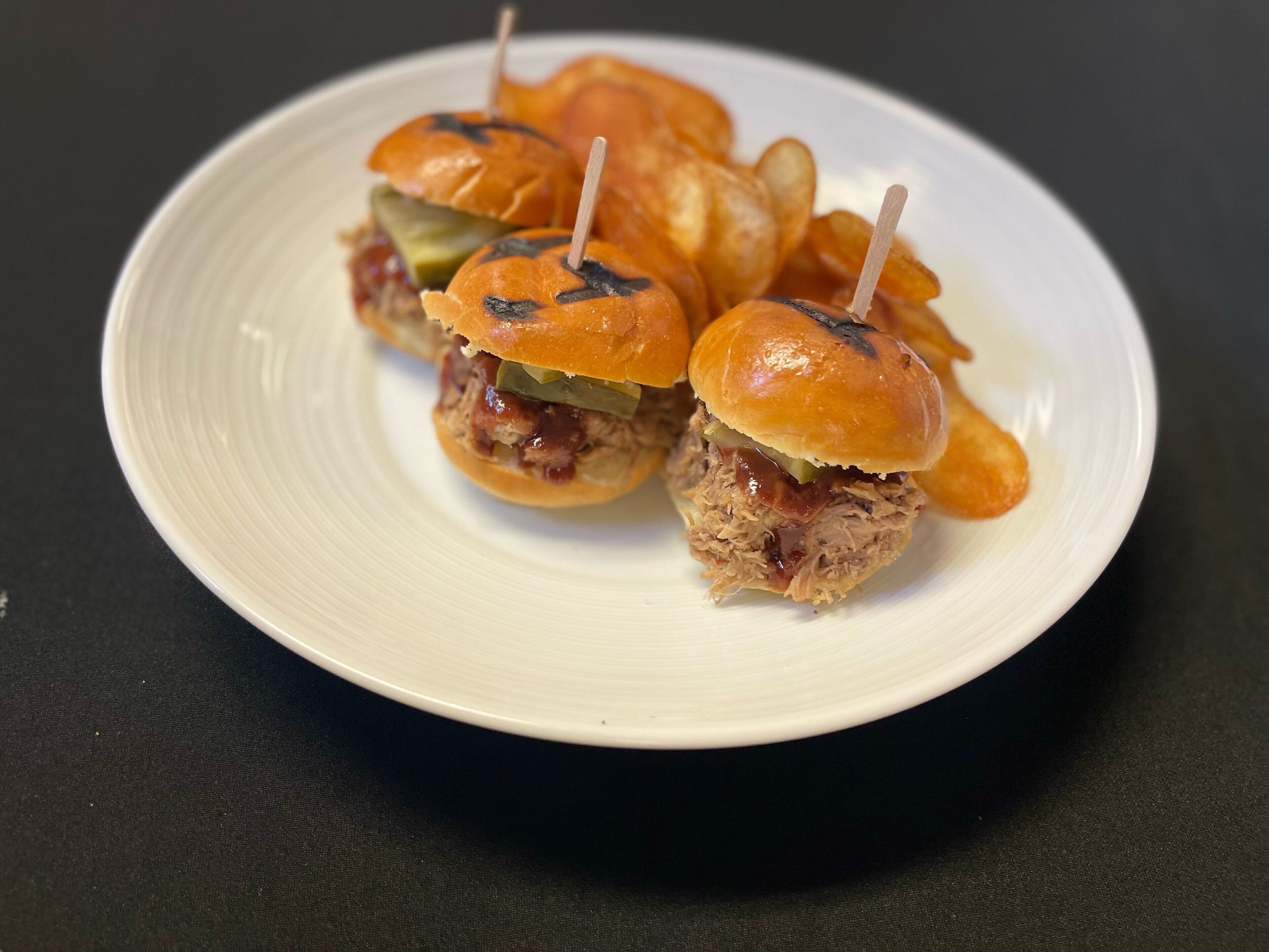 A white plate with three mini sandwiches on a dark surface.