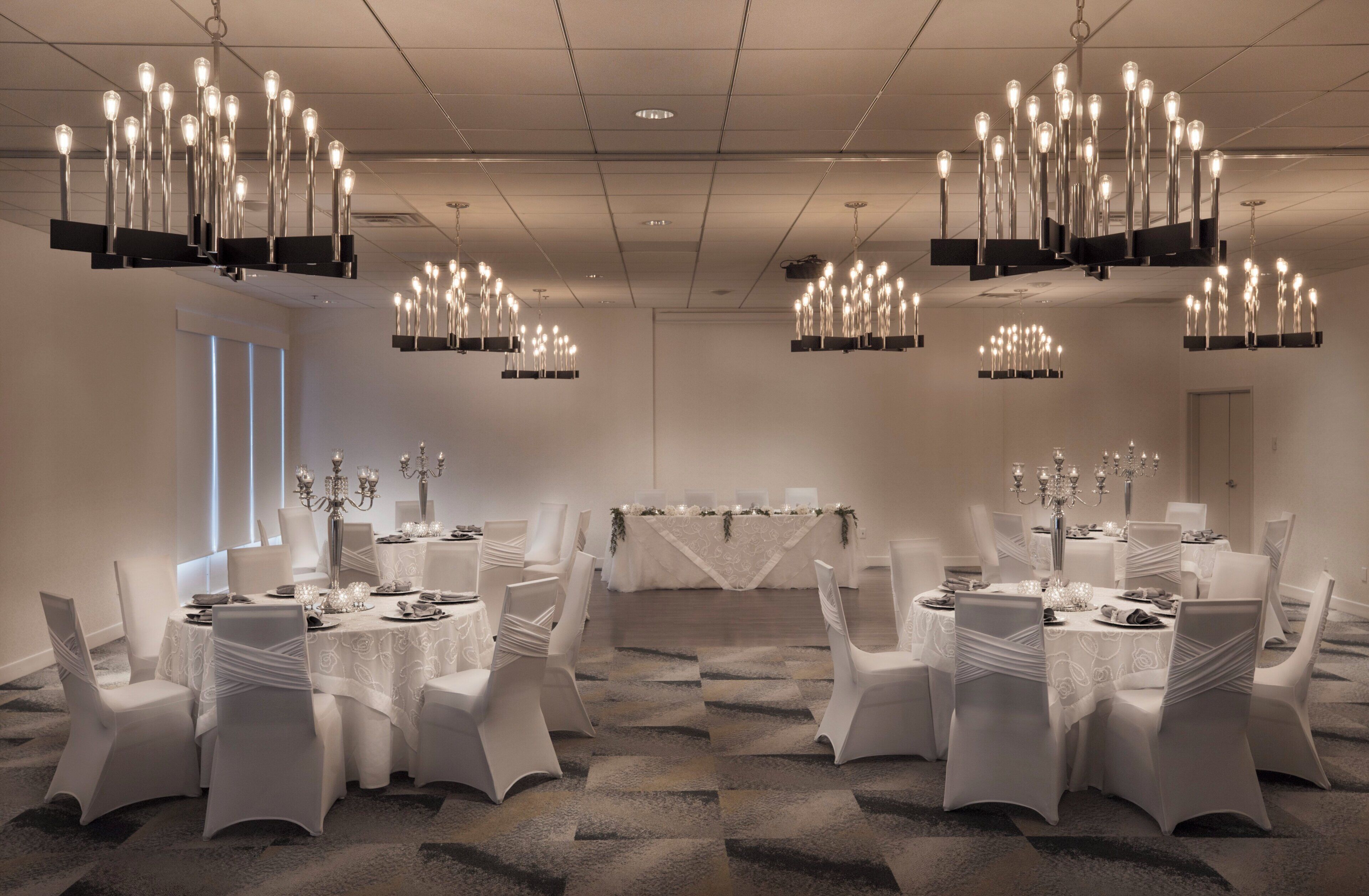 A conference room with multiple tables, white chairs, and chandeliers.