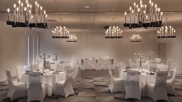 A conference room with multiple tables, white chairs, and chandeliers.