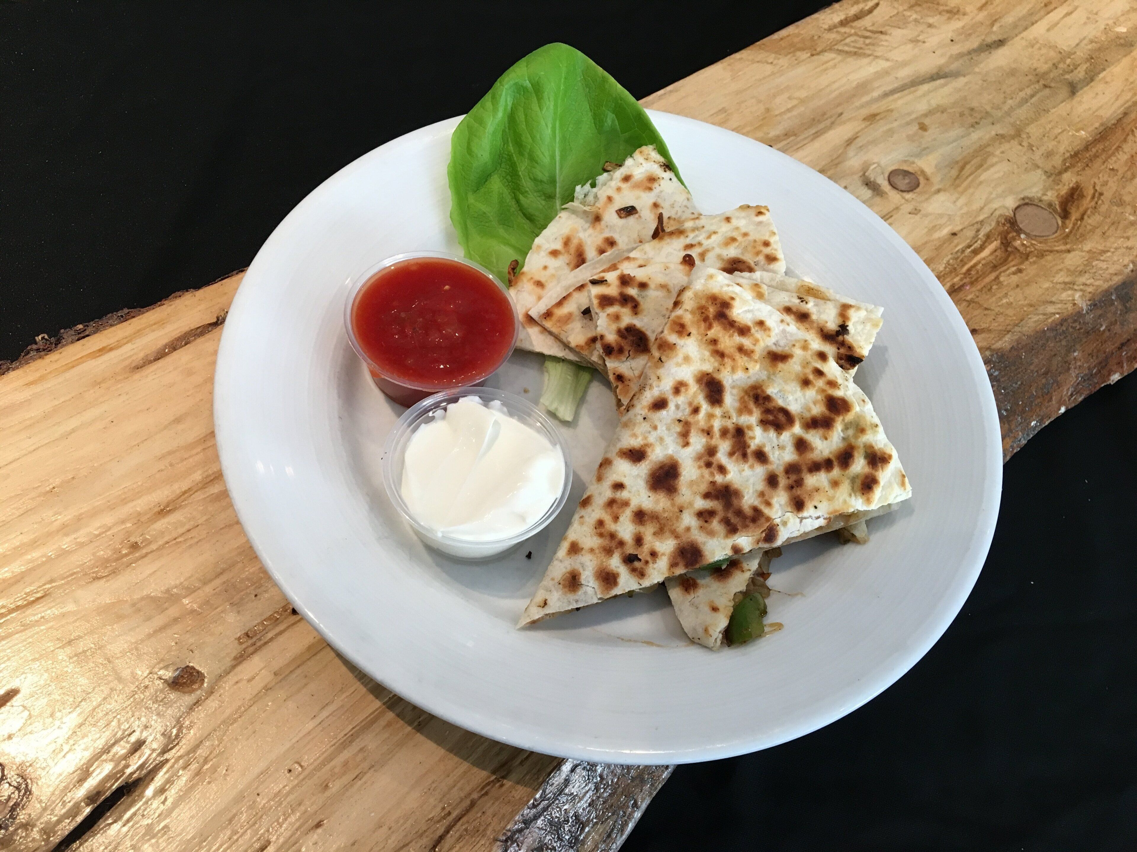 A plate with quesadillas, a side of sour cream, and a small bowl of salsa.
