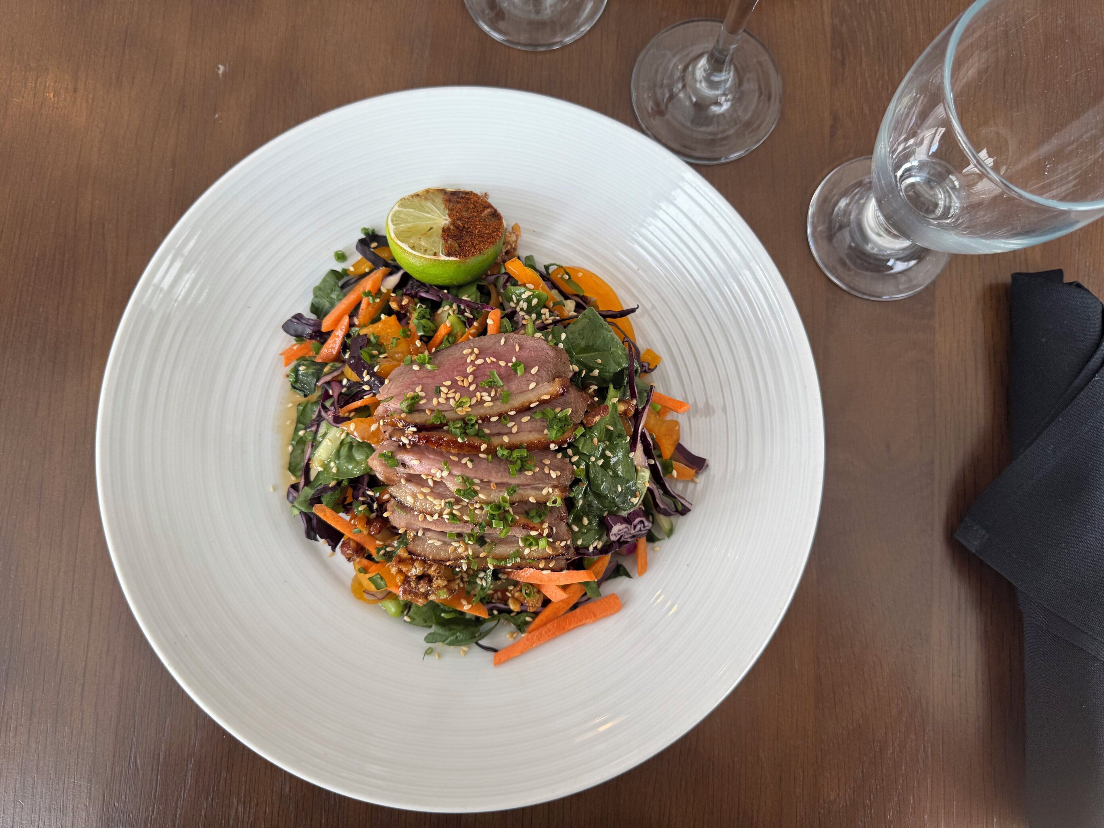 Een witte schaal met salade, een halve limoen en een glas water op een houten tafel.