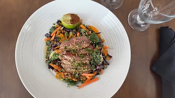 Une assiette blanche contenant une salade, une demi-lime et un verre d’eau, le tout posé sur une table en bois.