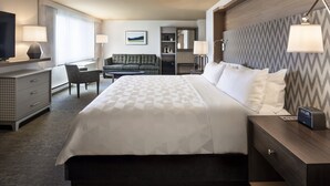 A hotel room with a large bed, a desk with a TV, a sofa, and a nightstand with a lamp. - Holiday Inn Montreal Longueuil by IHG (Longueuil)