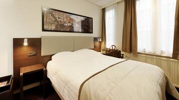 A hotel room with a large bed, a nightstand, a lamp, a painting on the wall, and a window with curtains.