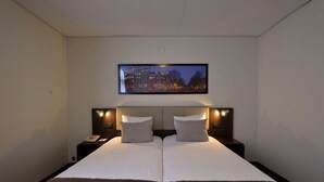 Habitación de hotel con una cama grande, dos mesitas de noche, un televisor de pantalla plana sobre la cama y vistas a la ciudad.