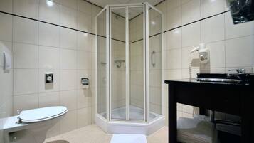 Un bany modern amb dutxa tancada amb vidre, un vàter i un lavabo amb mirall.
