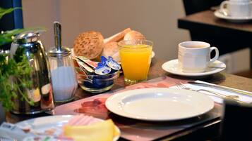 A breakfast setting with a pitcher, a glass of orange juice, a cup of coffee, bread rolls, and a plate with various food items.