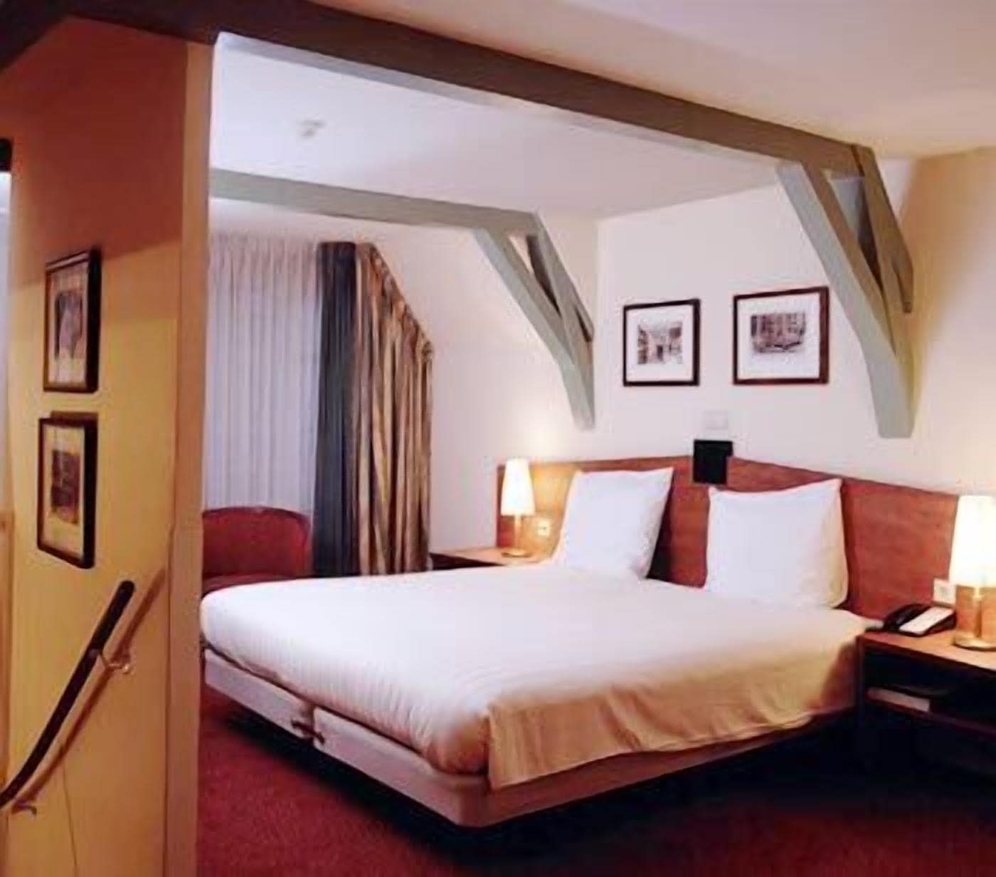 A hotel room with a bed, two bedside tables, a nightstand, a lamp, and framed pictures on the wall.