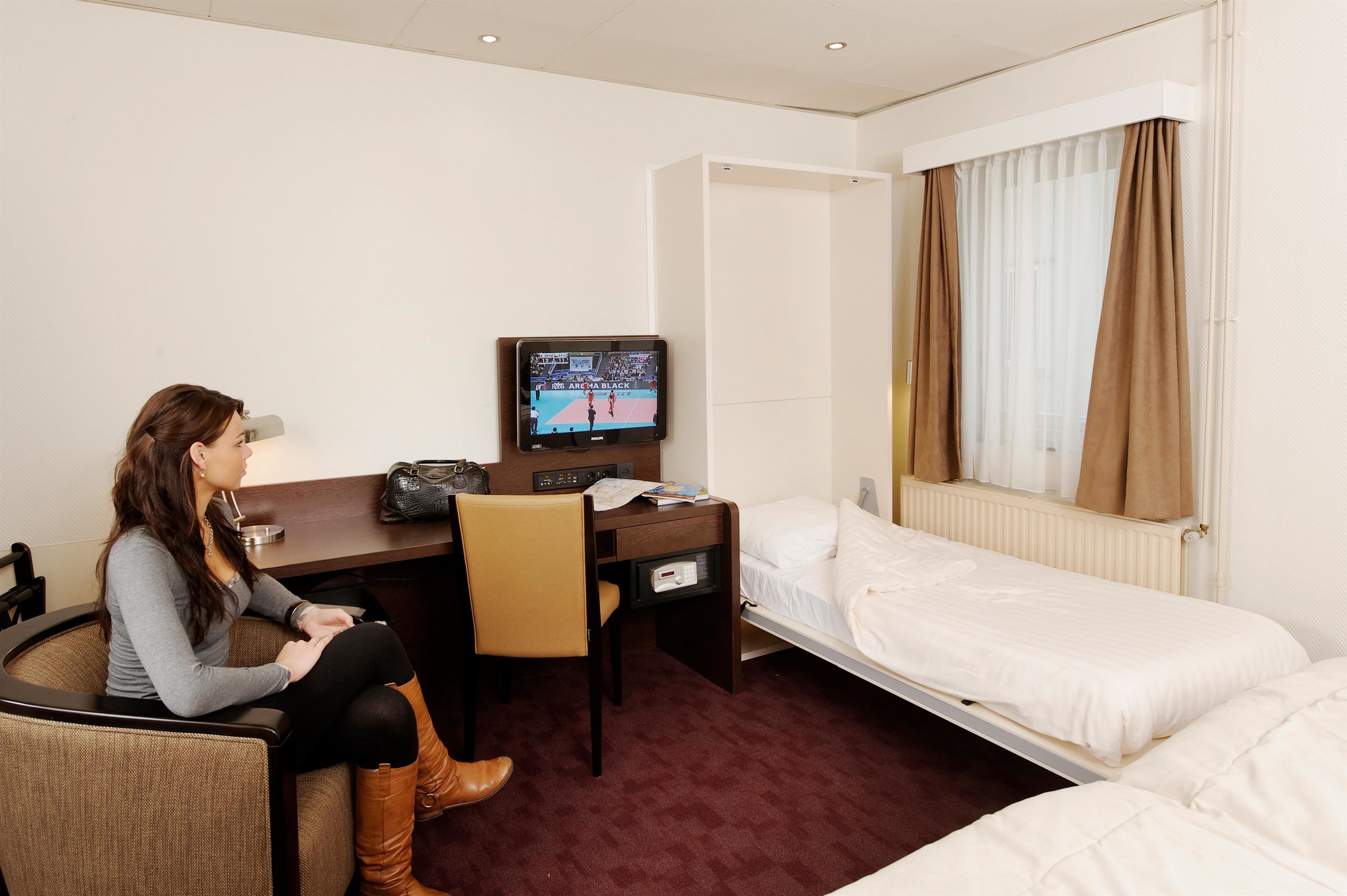 A hotel room with a single bed, a desk with a television, and a chair.