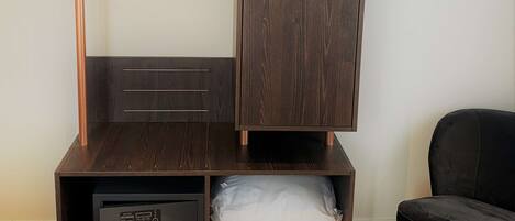A room with a dark wooden wardrobe, a small desk with drawers, and a hanging rack.