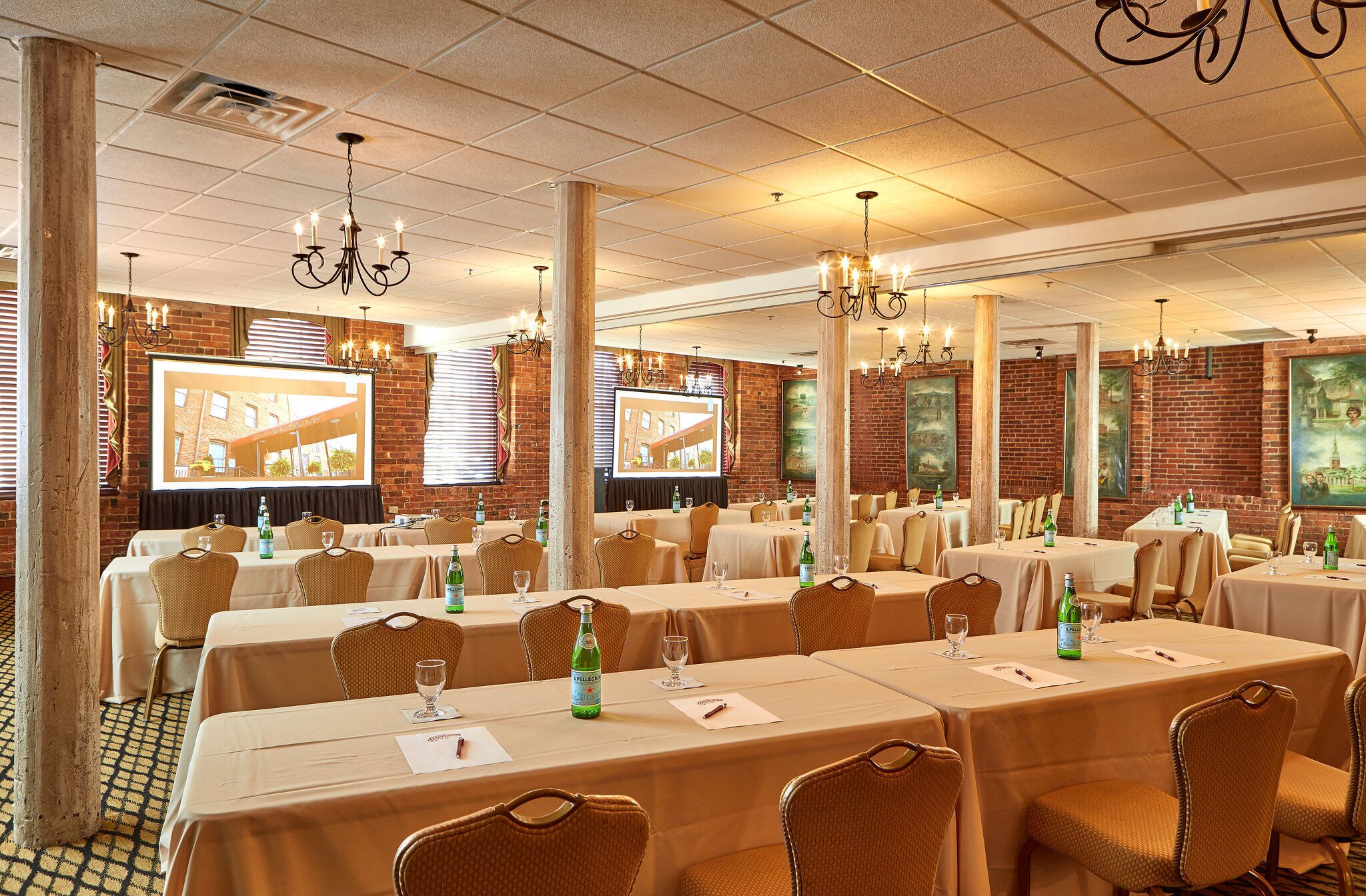 A conference room with multiple tables, chairs, and a large screen displaying a presentation.