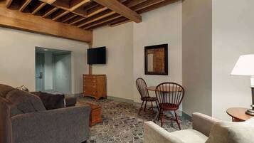 A cozy living room with a patterned carpet, wooden ceiling beams, a flat-screen TV, and a framed picture on the wall.