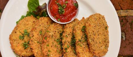 A plate of breaded and fried food items, possibly chicken cutlets, served with a side of fresh vegetables and a small bowl of sauce.