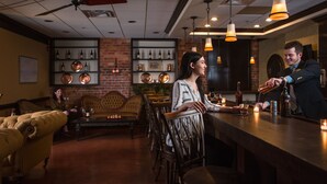 A bar area with wooden chairs, a bar counter, and shelves with bottles and glasses. - The Historic Brookstown Inn, Trademark Collection by Wyndham (Winston-Salem)
