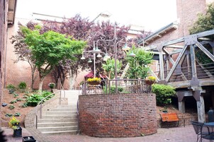 Un edificio de ladrillo con una escalera que lleva a un balcón, mobiliario exterior y una estructura de escalera de metal.