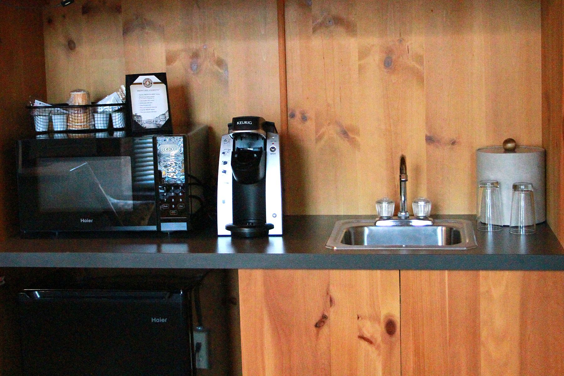 Een keuken met een magnetron, koffiezetapparaat en een spoelbak.