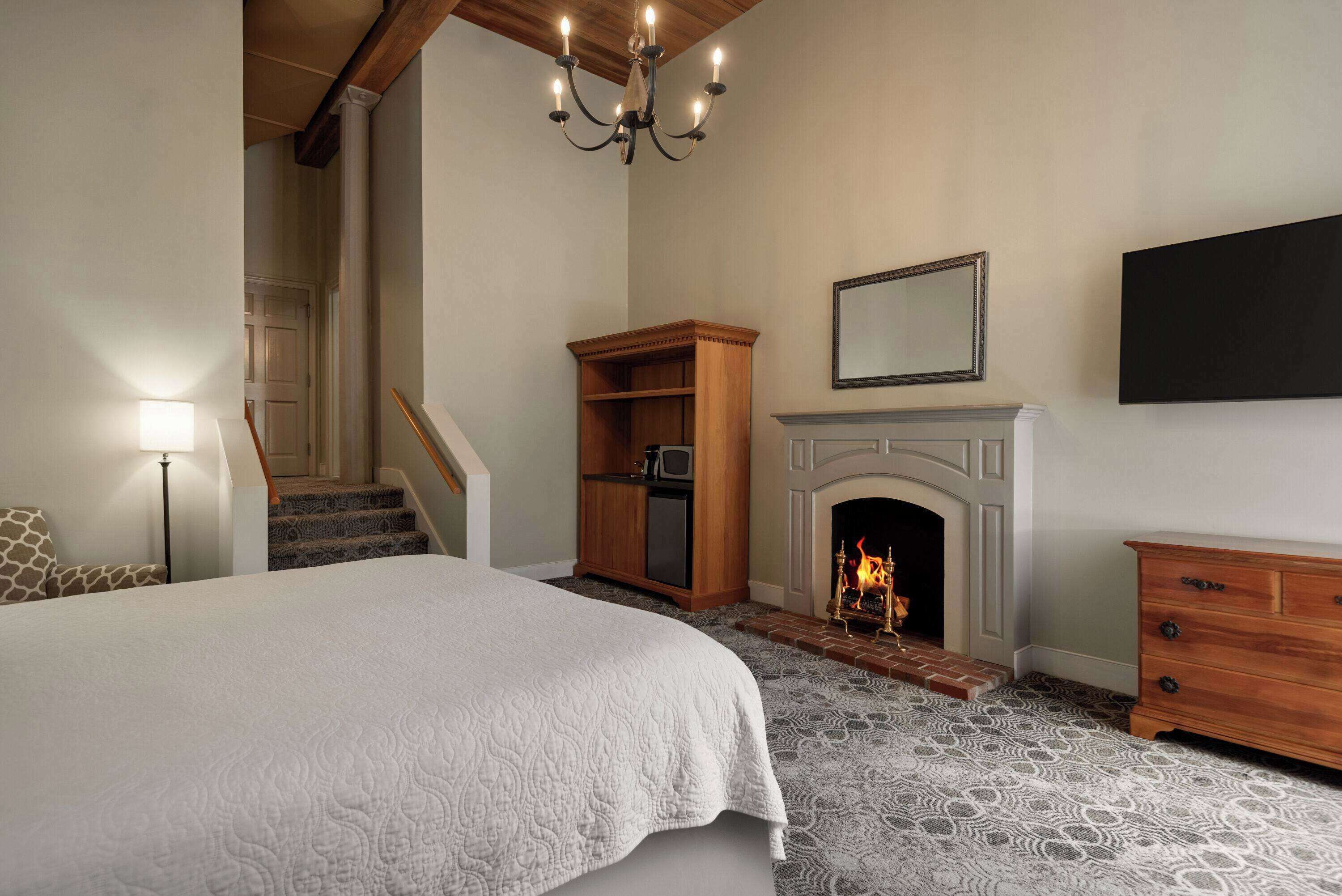 A bedroom with a large bed, a fireplace, a wooden cabinet, and a staircase.