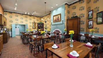 Un comedor con suelo de ladrillo, mesas y sillas de madera, y papel tapiz floral amarillo.