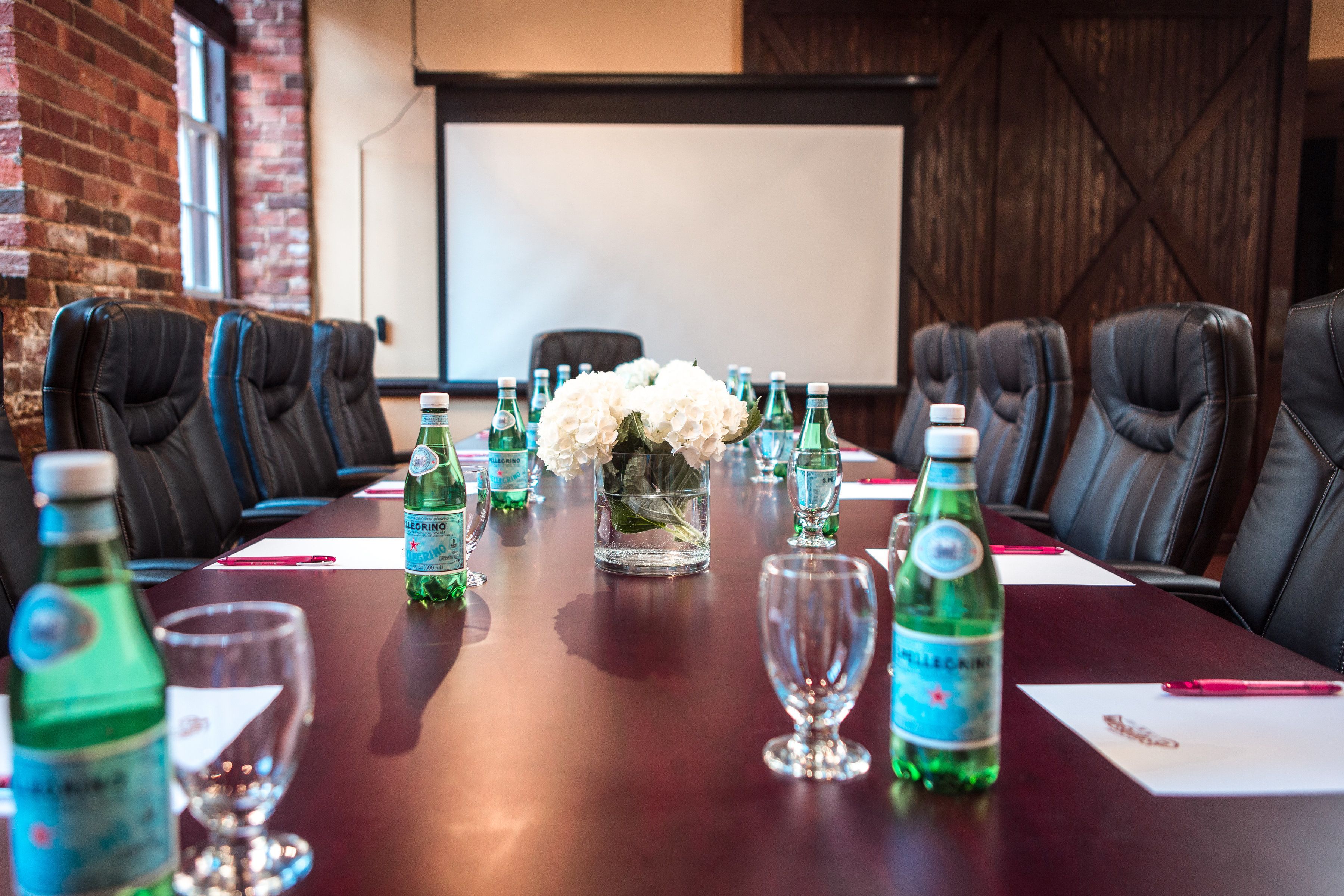 A conference room with a long table, multiple chairs, and a projector screen in the background.