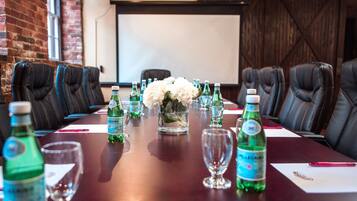 A conference room with a long table, multiple chairs, and a projector screen in the background.