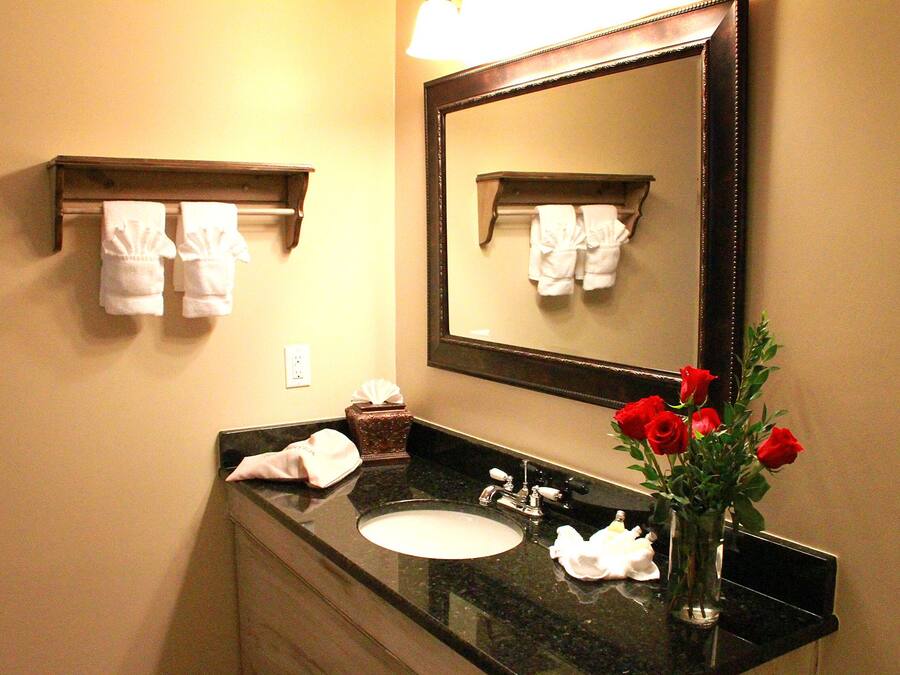 A bathroom with a sink, mirror, towel rack, and a vase with red roses.