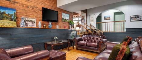 A spacious living room with a brick wall, leather sofas, a wooden coffee table, and a staircase leading to another level.