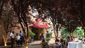 An outdoor patio area with brick flooring, tables and chairs, and a building entrance with a red awning. - The Historic Brookstown Inn, Trademark Collection by Wyndham (Winston-Salem)