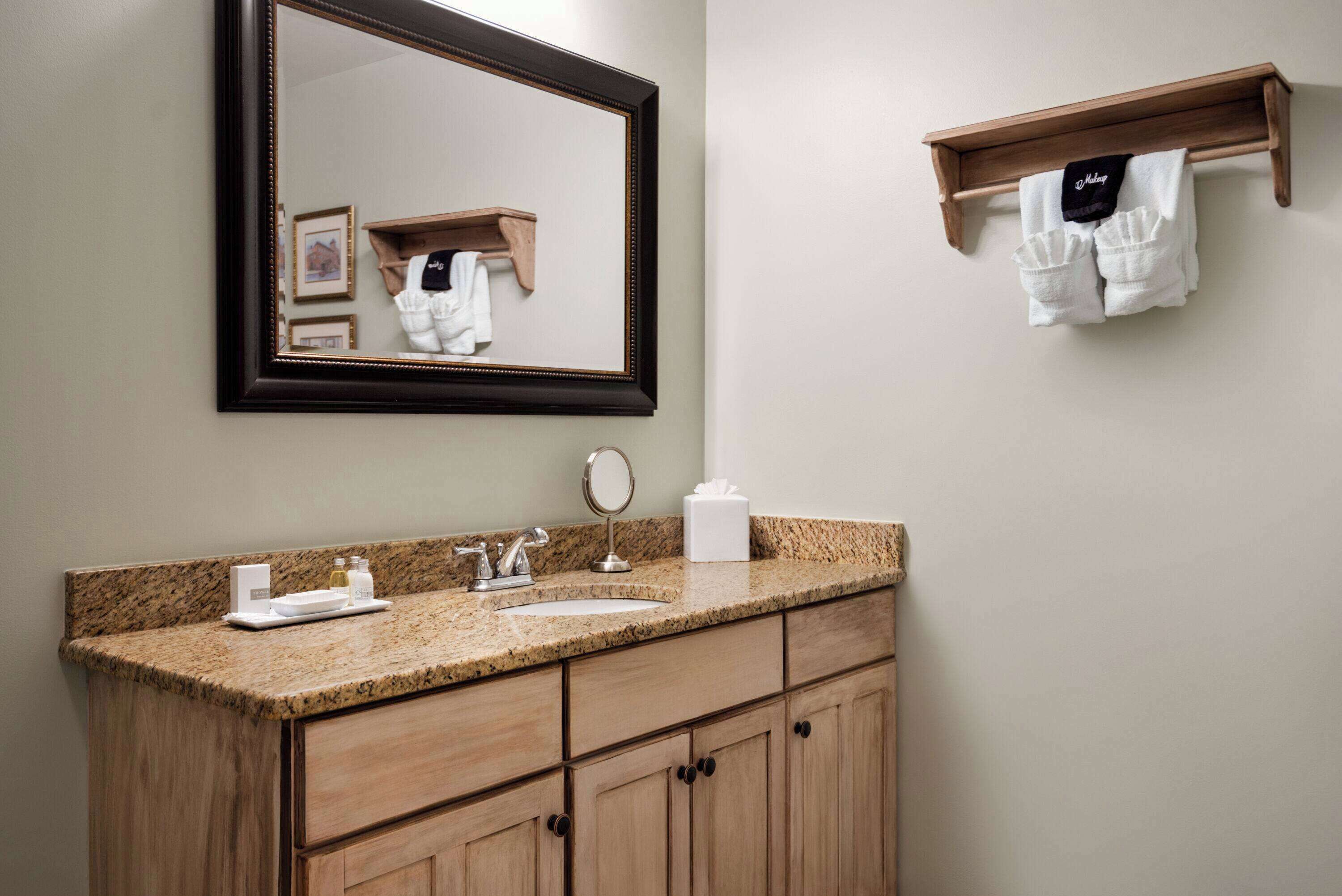 A bathroom with a granite countertop, a sink, a mirror, and wooden cabinets.