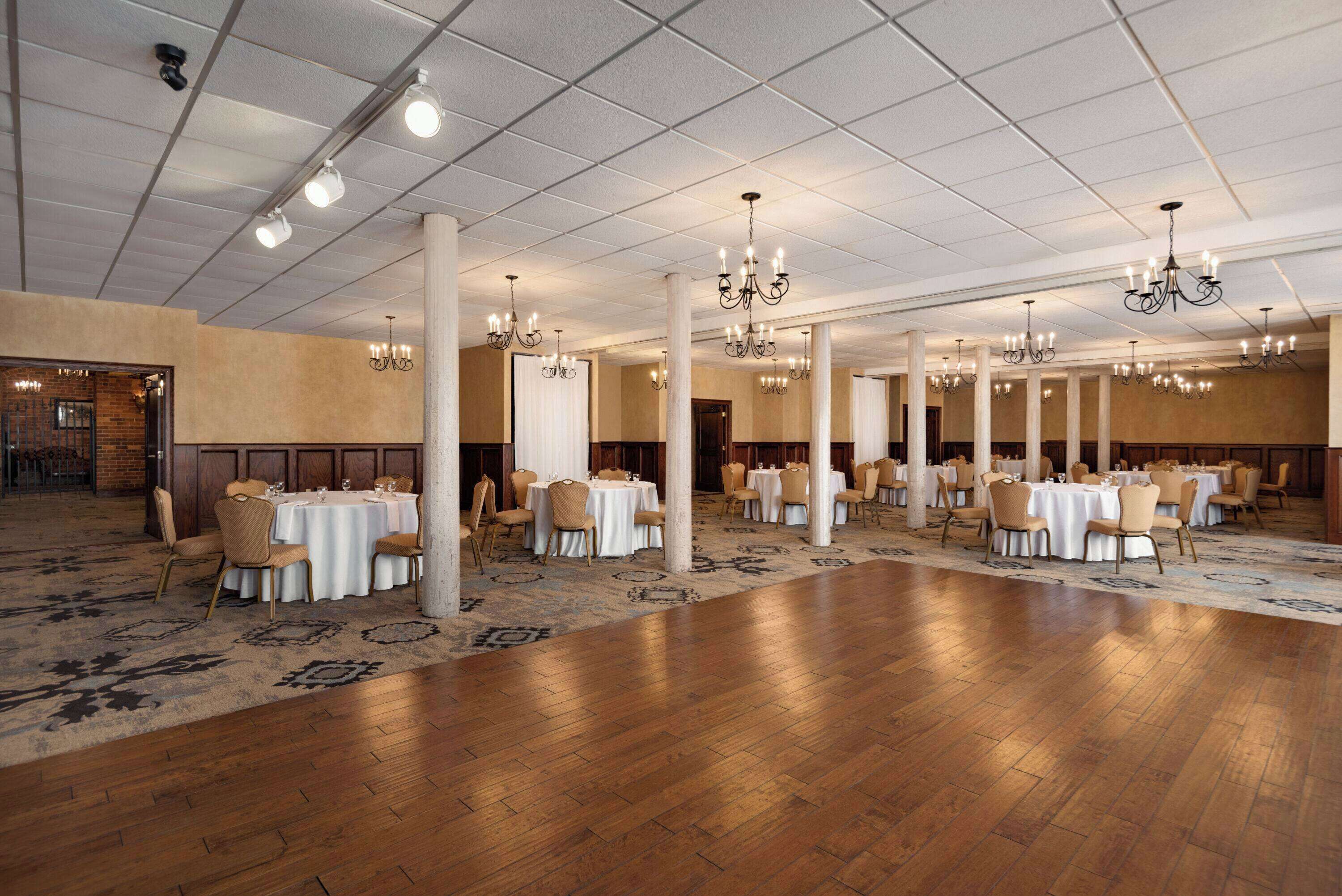 Een ruime balzaal met meerdere ronde tafels en stoelen, witte draperieën en kroonluchters.