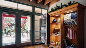 A hotel lobby with a wooden reception desk, a refrigerator, a shelf with various items, and a view of the outdoor area through glass doors. - The Historic Brookstown Inn, Trademark Collection by Wyndham (Winston-Salem)