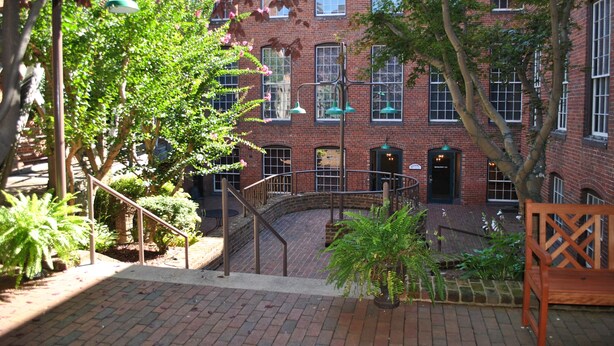 A courtyard with brick buildings, a staircase, and potted plants. - The Historic Brookstown Inn, Trademark Collection by Wyndham (Winston-Salem)