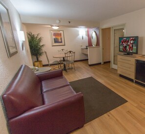 A living room with a red sofa, a dining table with chairs, a TV on a stand, and a potted plant. - Red Roof Inn Hilton Head Island (Hilton Head Island)