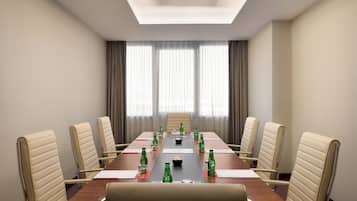 Un salón de conferencias con una larga mesa, sillas color beige y botellas verdes sobre la mesa.