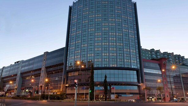 Un hotel moderno con fachada curva, varios pisos y un llamativo letrero de "RAMADA" en la parte superior.