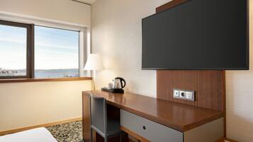 Habitación de hotel con escritorio, silla, televisión, lámpara y vistas a la ciudad.