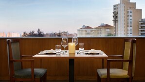 Una mesa de comedor preparada con una vela, vasos y cubiertos, con vistas a la ciudad al fondo.