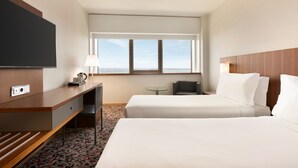Habitación de hotel con una cama grande, un escritorio con televisor de pantalla plana, una silla, una mesita y una ventana con vistas.