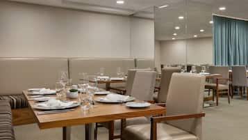A dining area with wooden tables, beige chairs, and a large mirror on the wall.