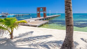 A beach scene with a palm tree, clear blue sky, and a pier extending into the ocean. - Sunbreeze Hotel (San Pedro)