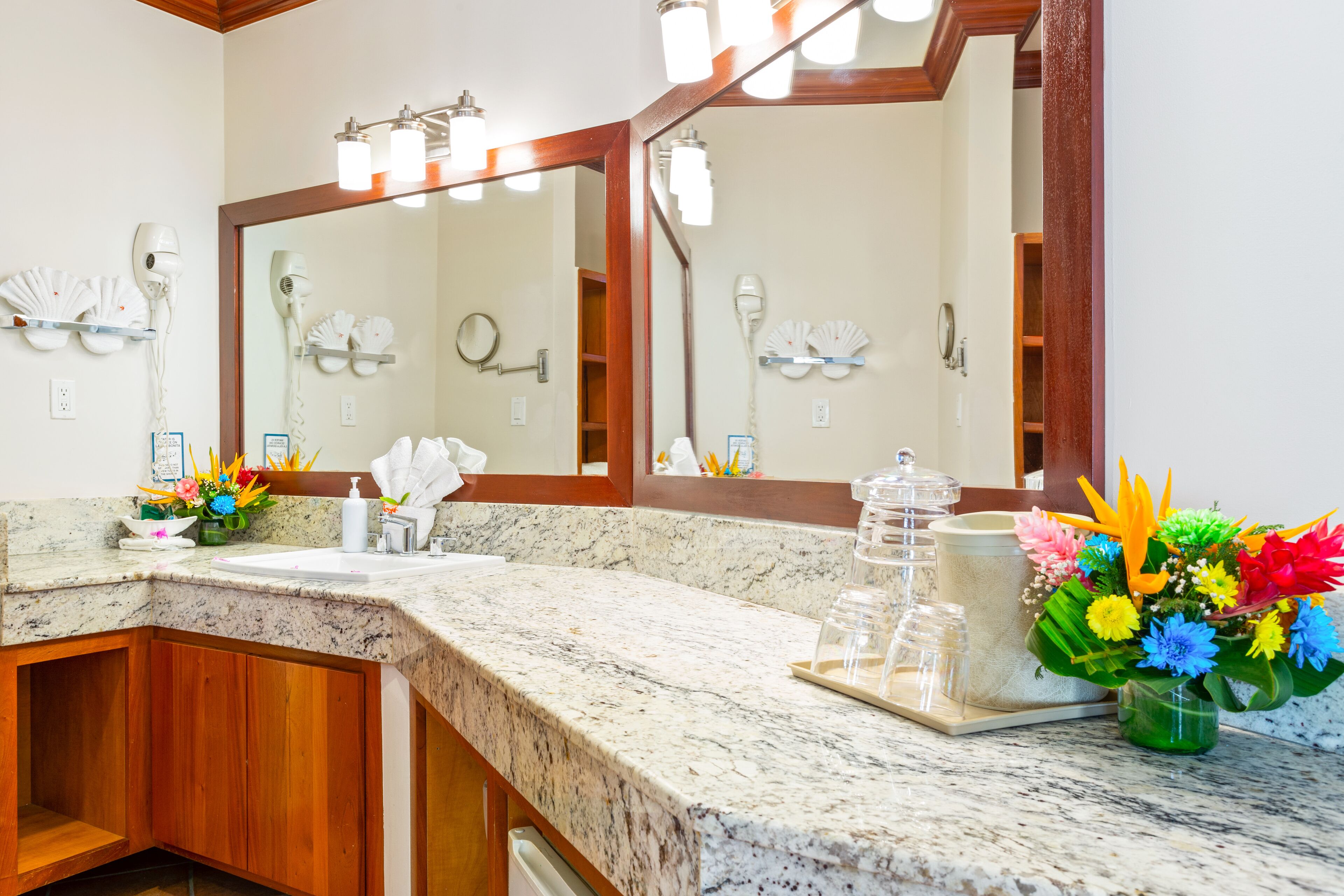 Un baño con encimera de granito, un espejo grande y un jarrón con flores.