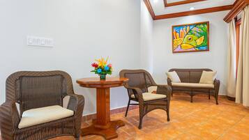 A room with two wicker chairs, a small round table with a vase of flowers, and a colorful fish painting on the wall.